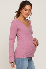 woman wearing a pink long sleeve maternity top and gently holding her baby bump