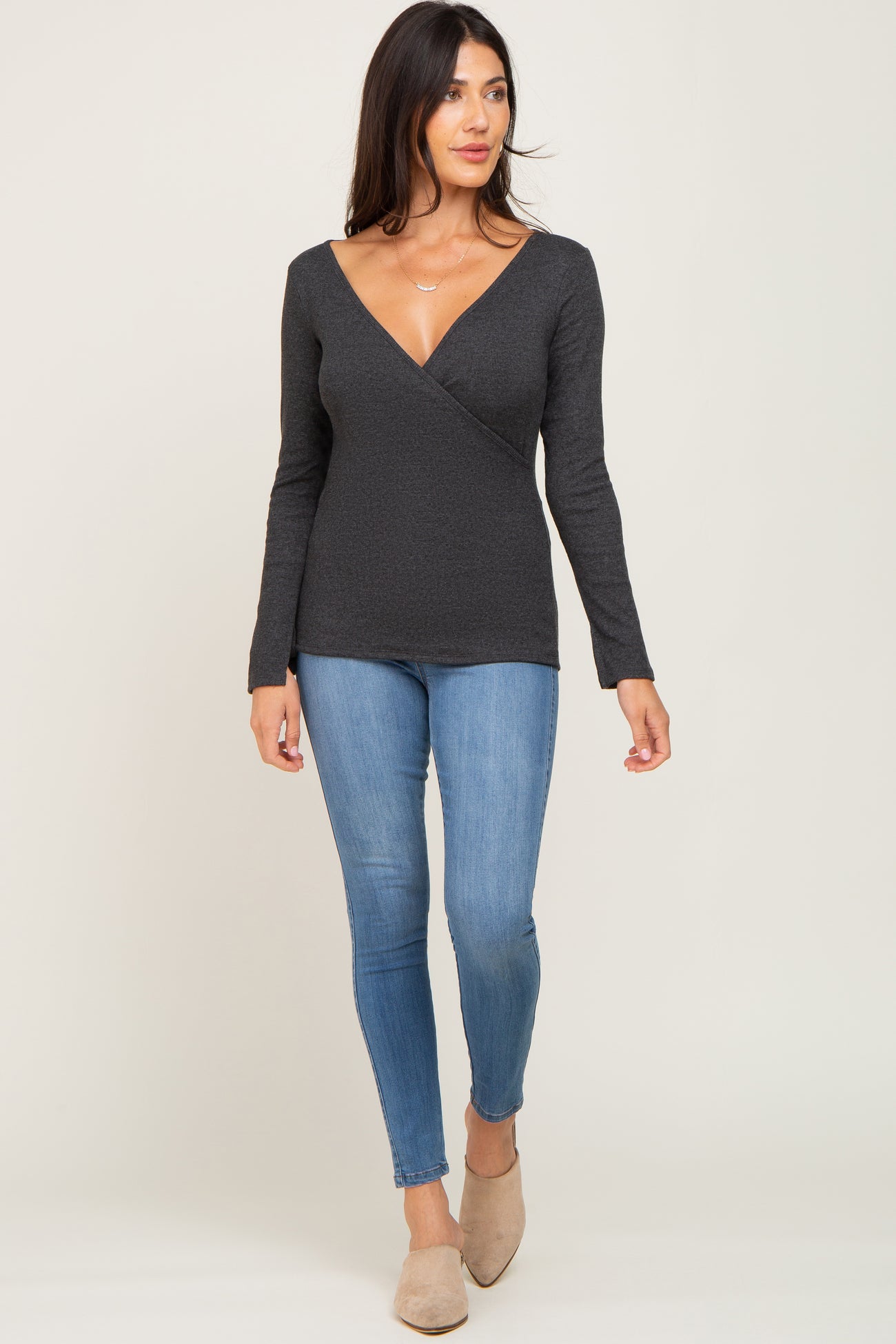 woman wearing a charcoal grey long sleeve surplice top and blue skinny jeans with tan mules