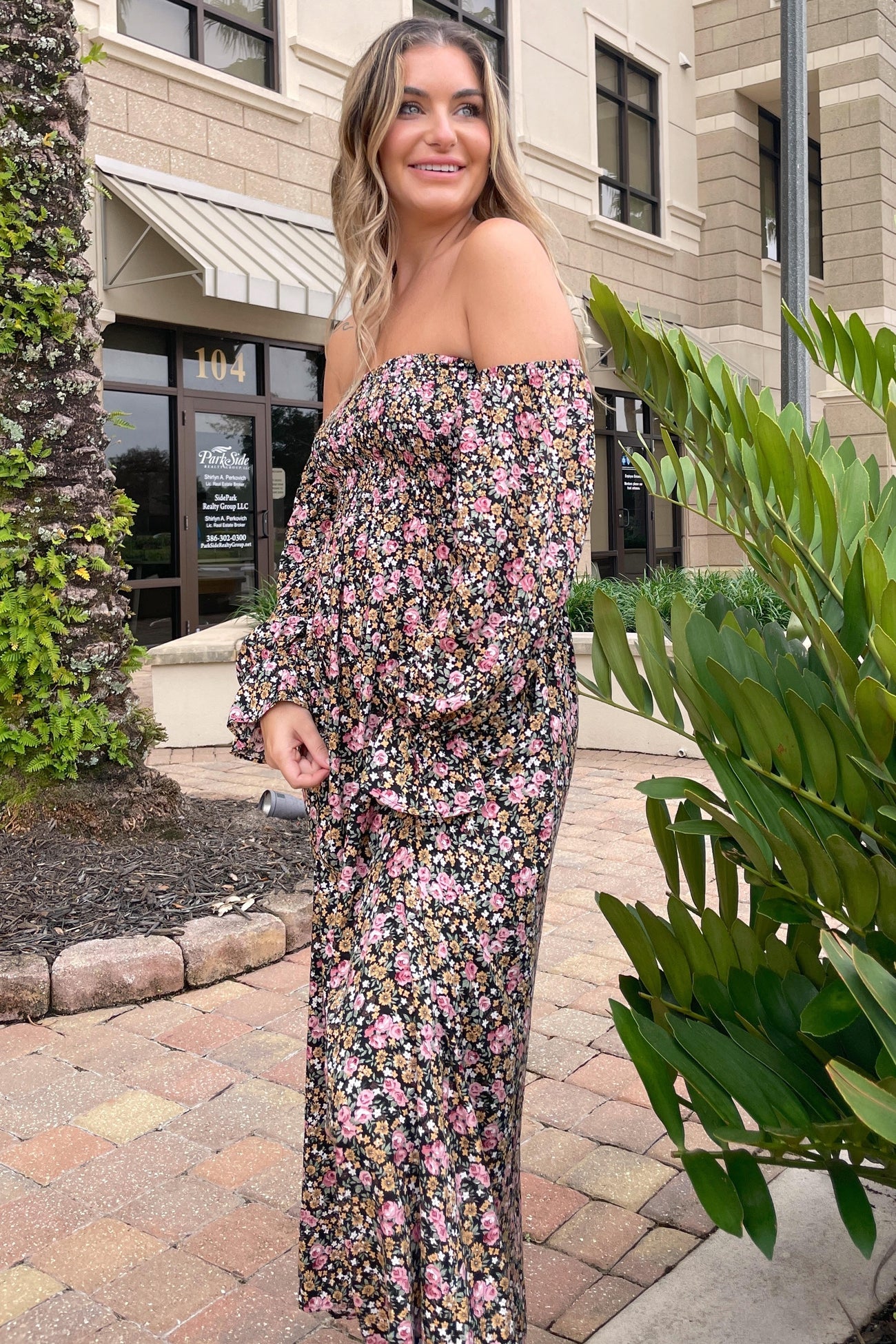 woman wearing a black floral off-the-shoulder maternity dress with long sleeves and a relaxed fit, standing outdoors