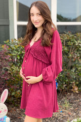 woman wearing a burgundy maternity dress with lace detail and a visible baby bump, standing outdoors