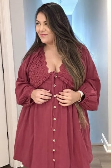 woman wearing a burgundy button-up dress with lace detailing and long sleeves, standing in a hallway