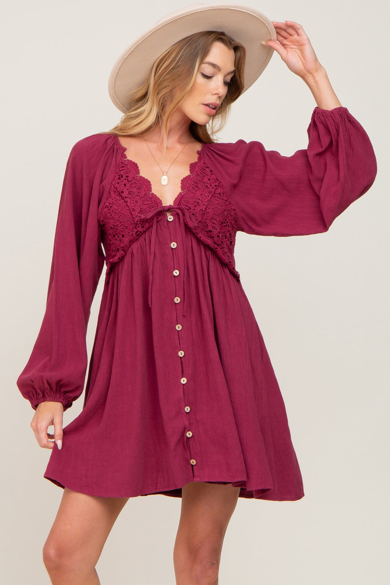 woman wearing a burgundy button-up dress with lace details and long sleeves, accessorized with a wide-brimmed hat