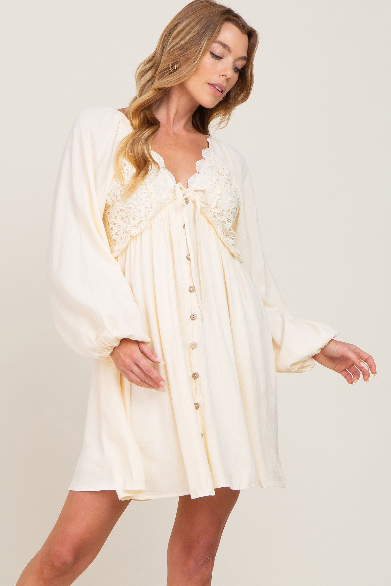 woman wearing a cream long sleeve mini dress with lace bodice and button front detail