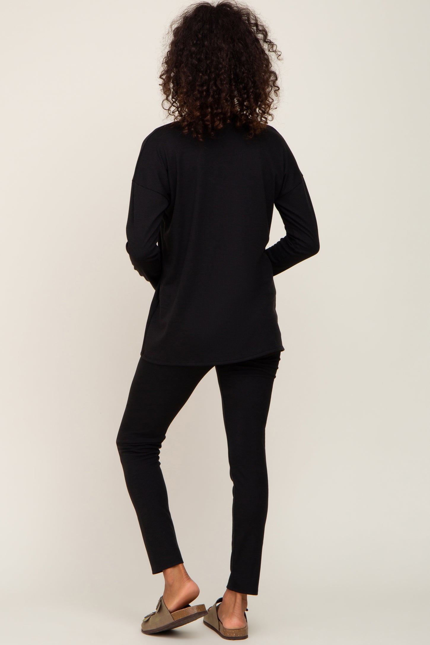 woman with curly hair from behind wearing black long sleeve ribbed top and matching leggings with sandals