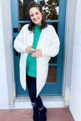smiling pregnant woman in green sweater and white cardigan standing in front of a blue door