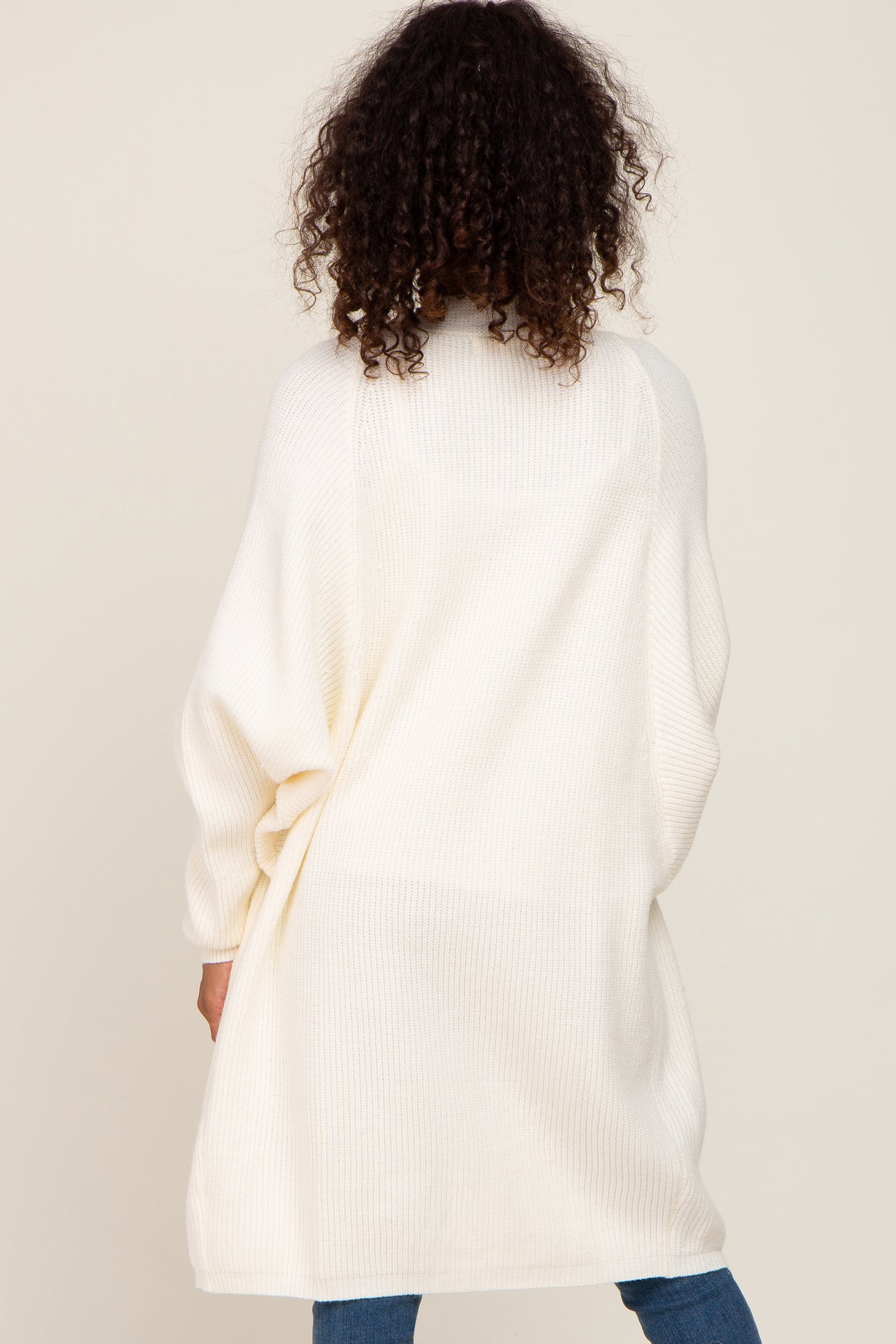woman wearing an oversized white knitted cardigan, seen from the back, paired with blue jeans