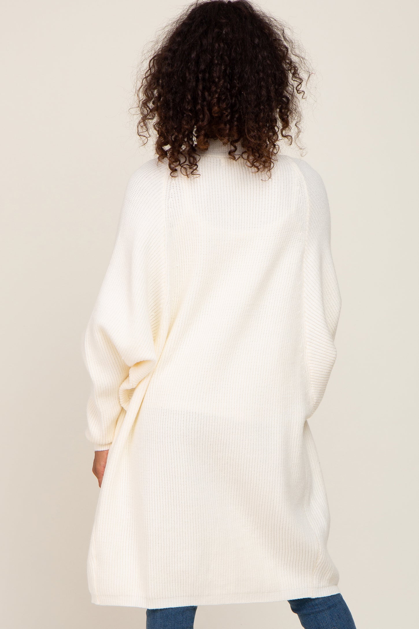 woman wearing an oversized white knitted cardigan, seen from the back, paired with blue jeans