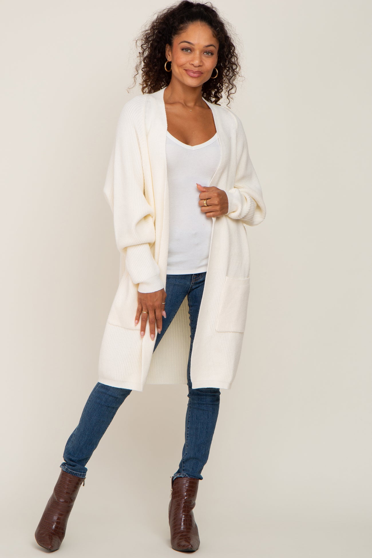 woman wearing a cream open-front cardigan over a white top paired with blue skinny jeans and brown ankle boots