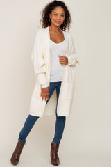 woman wearing a cream open-front cardigan over a white top paired with blue skinny jeans and brown ankle boots