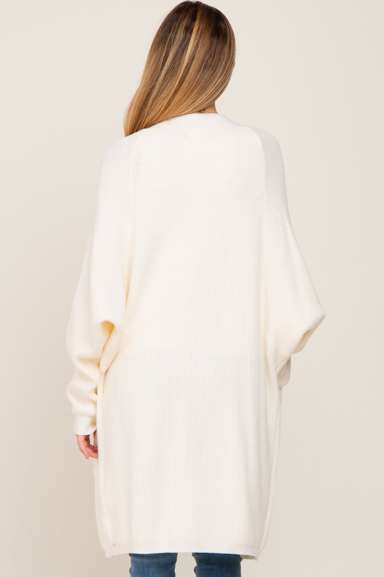 woman wearing a cream oversized maternity cardigan with long sleeves, shown from the back