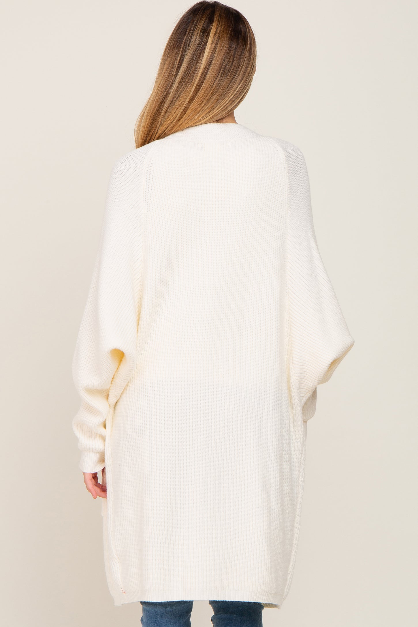 woman wearing a cream oversized maternity cardigan with long sleeves, shown from the back