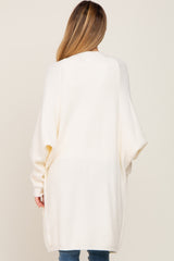 woman wearing a cream oversized maternity cardigan with long sleeves, shown from the back