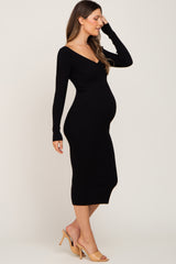 Pregnant woman wearing a black long-sleeve ribbed maternity midi dress and tan heels against a neutral background.