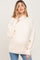 woman wearing a cream ribbed maternity sweater with a mock neck and button details on the sleeves