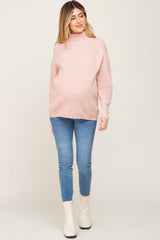 pregnant woman wearing a pink turtleneck maternity sweater and blue jeans with white boots
