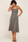 woman wearing a sage green midi dress with smocked bodice and wide adjustable straps, standing and smiling