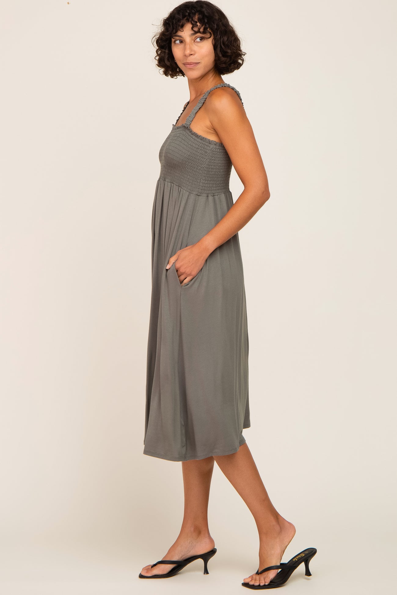 woman wearing a dusty green sleeveless midi dress with smocked bodice and side pockets