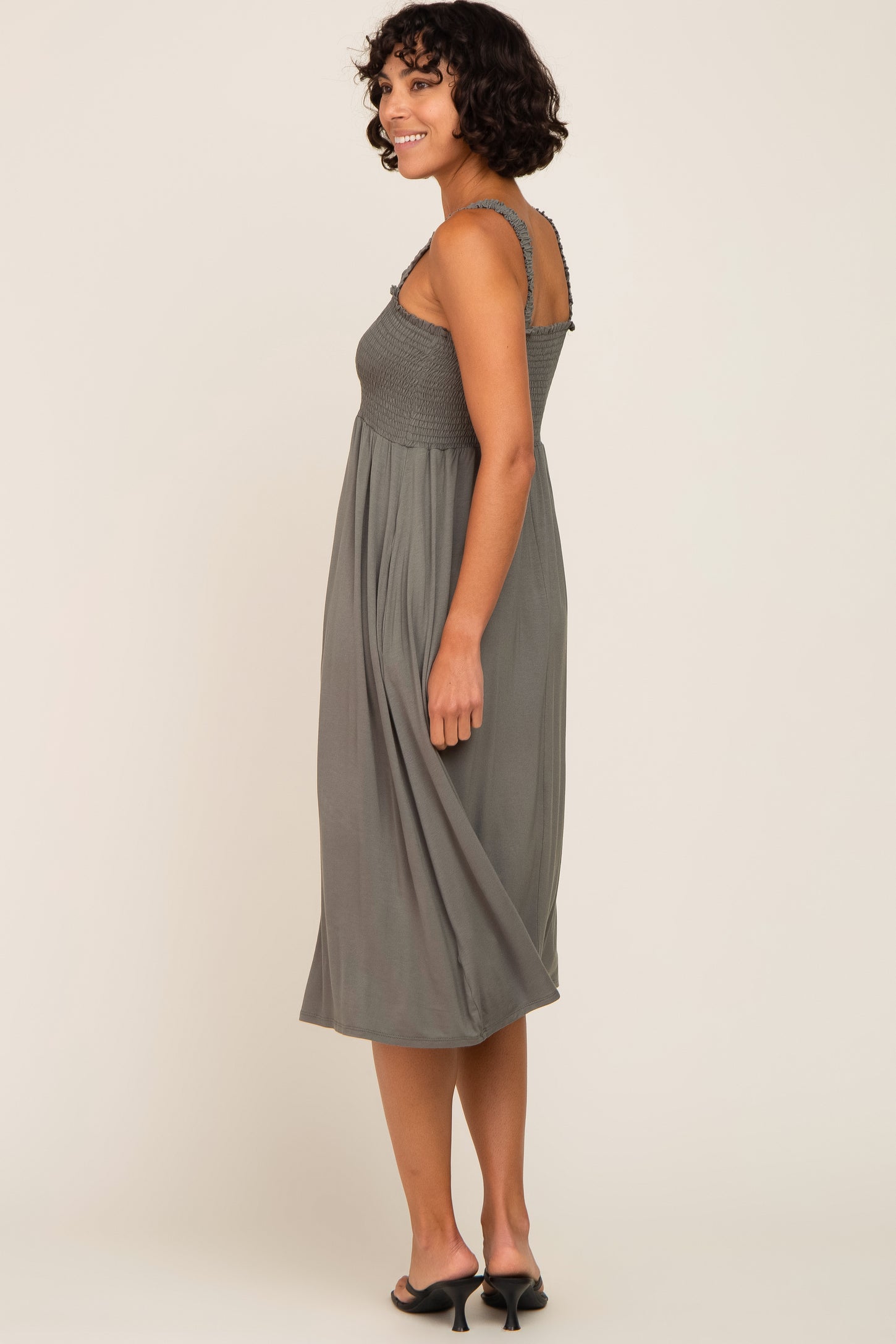 woman wearing a gray smocked midi dress with a flowy skirt and spaghetti straps, shown from the side