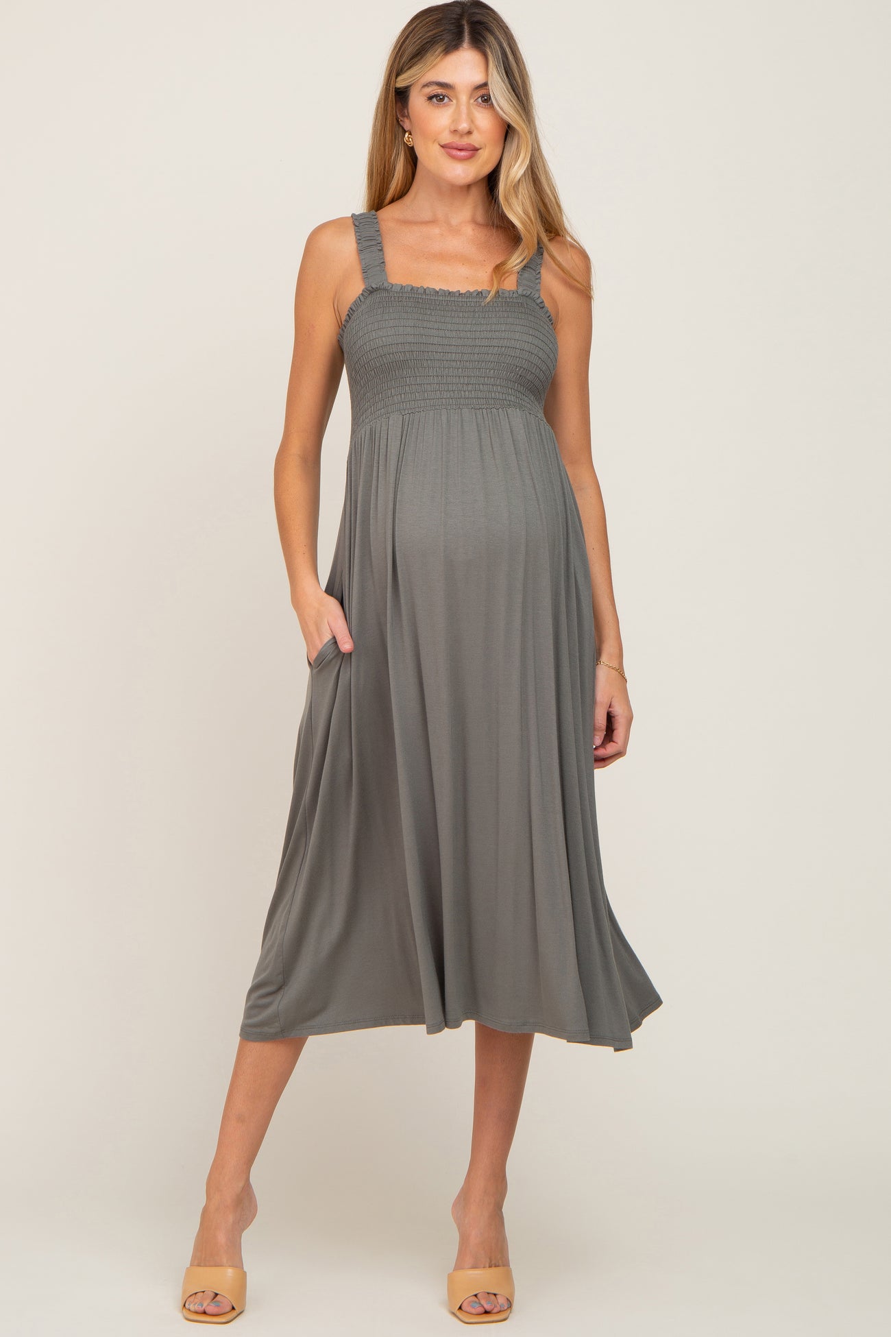 woman wearing a gray maternity dress with smocked bodice and pockets, highlighting her baby bump.