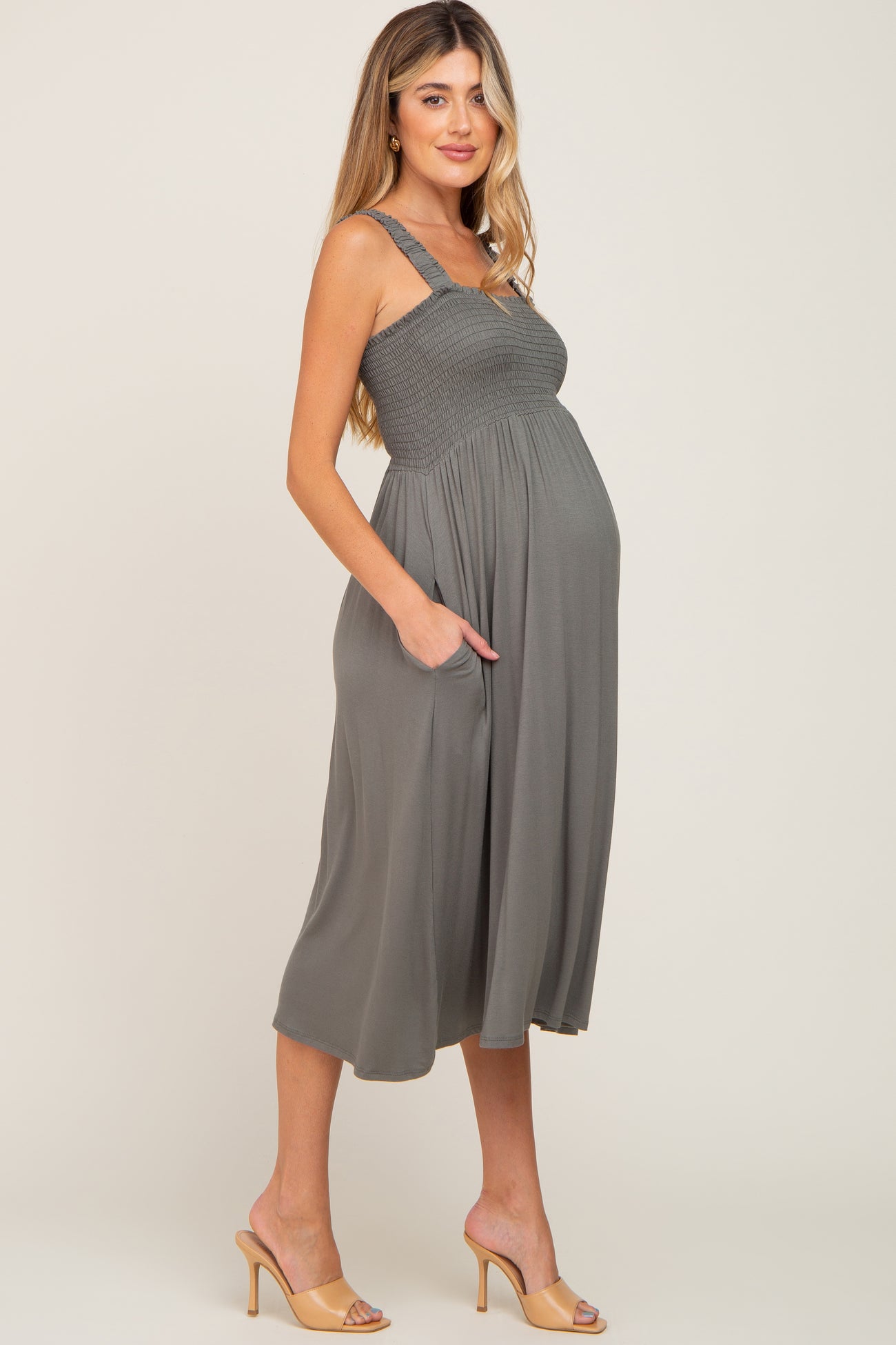 woman wearing a slate gray maternity dress with smocked bodice and pockets, showcasing her baby bump