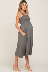 woman wearing a slate gray maternity dress with smocked bodice and pockets, showcasing her baby bump