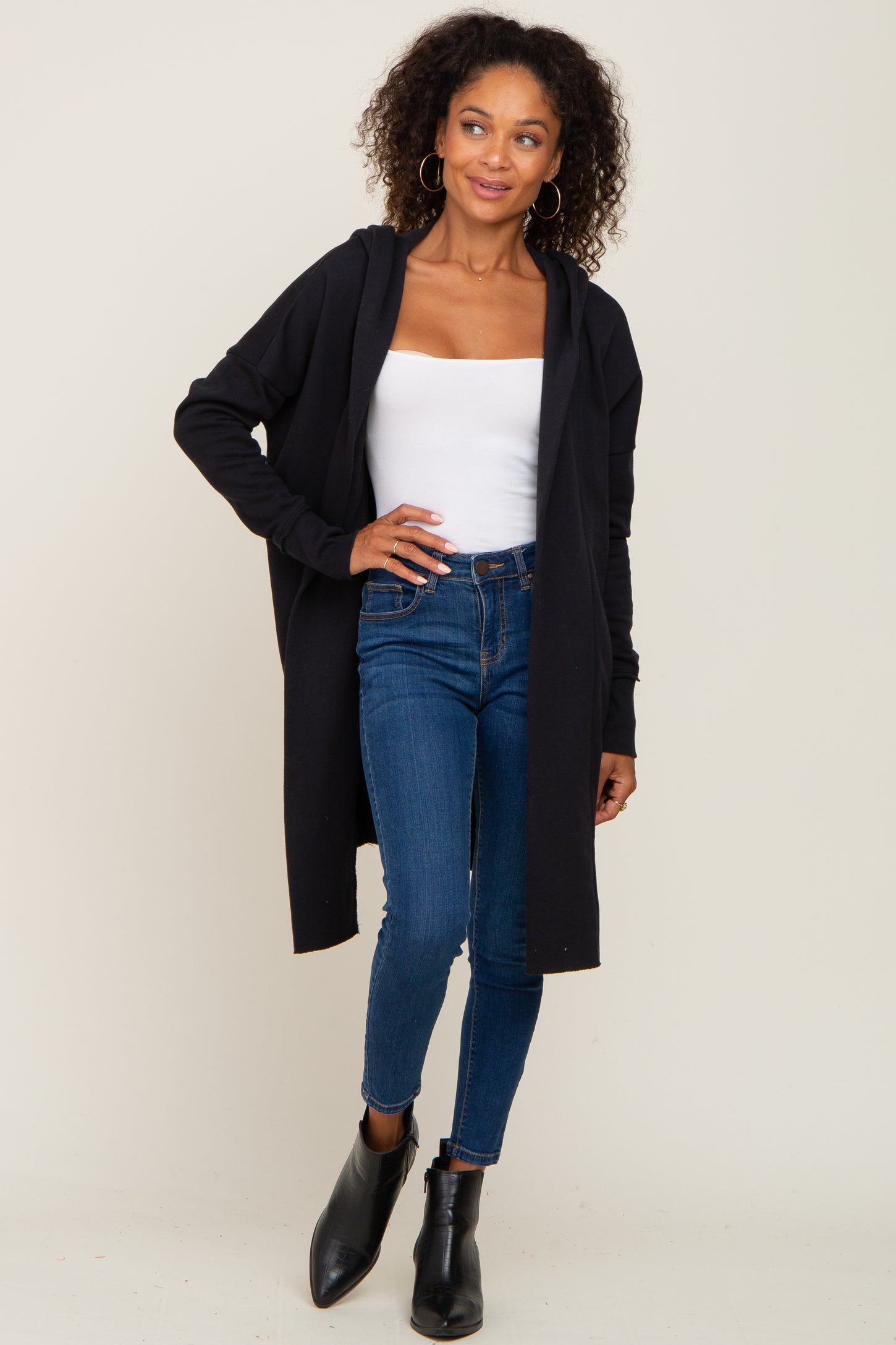 woman wearing a black longline cardigan over a white tank top and blue skinny jeans with black ankle boots