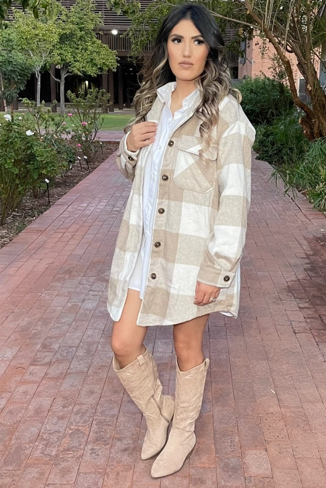 Woman wearing a beige and white plaid shacket with tan cowboy boots on a brick walkway
