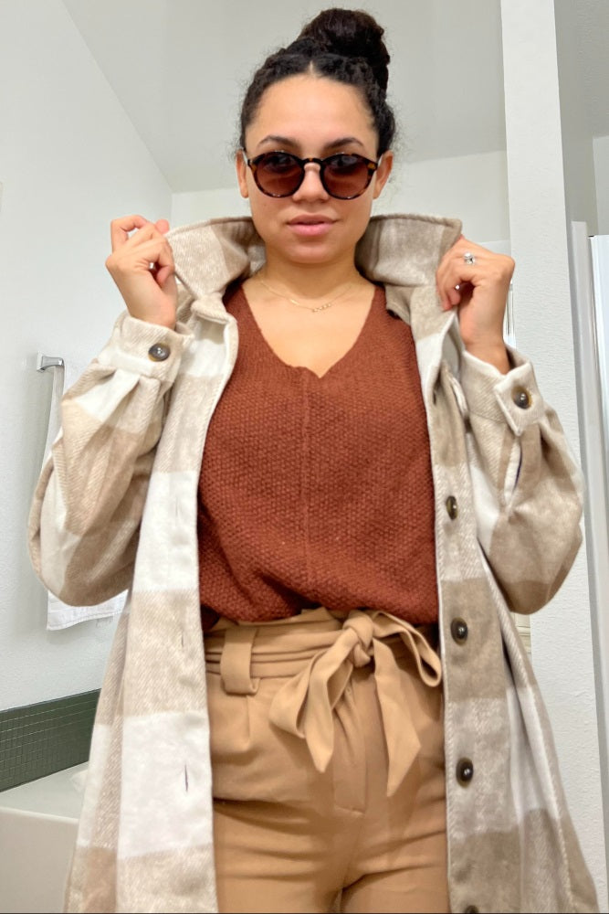Woman wearing a tan plaid shacket over a rust orange sweater and paperbag waist trousers with sunglasses.