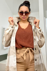 Woman wearing a tan plaid shacket over a rust orange sweater and paperbag waist trousers with sunglasses.