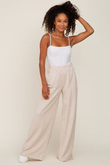 woman wearing white spaghetti strap bodysuit and beige wide leg sweatpants against a neutral background