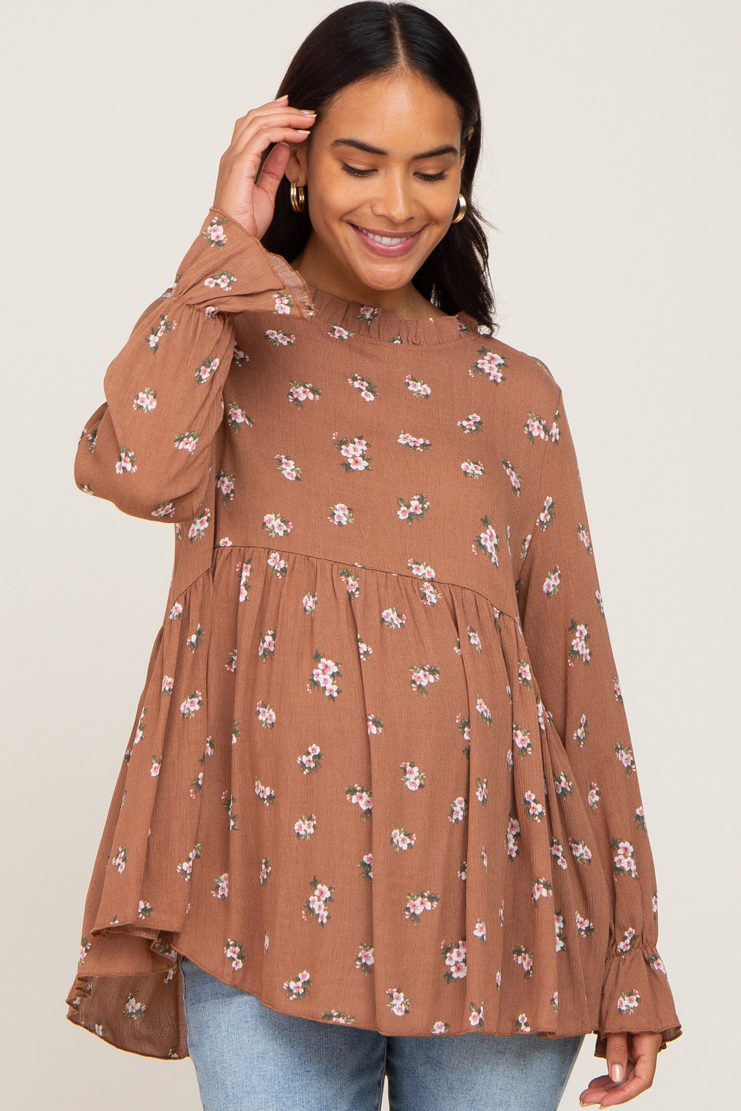 woman wearing a brown floral maternity top with long sleeves and a flowy silhouette, smiling while holding her baby bump