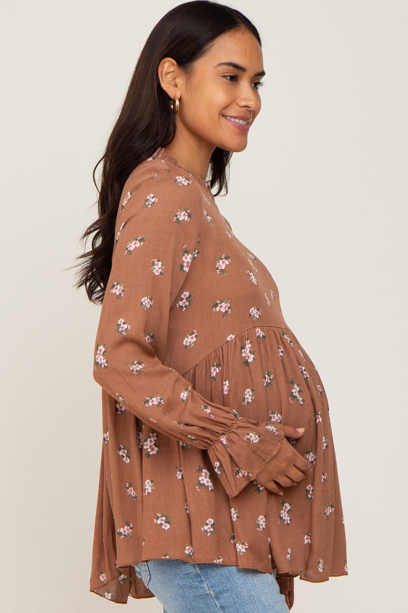 woman wearing a brown floral maternity top and holding her baby bump