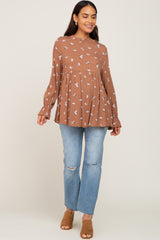 woman wearing a brown floral maternity top with a flowing silhouette and bell sleeves paired with distressed light blue jeans