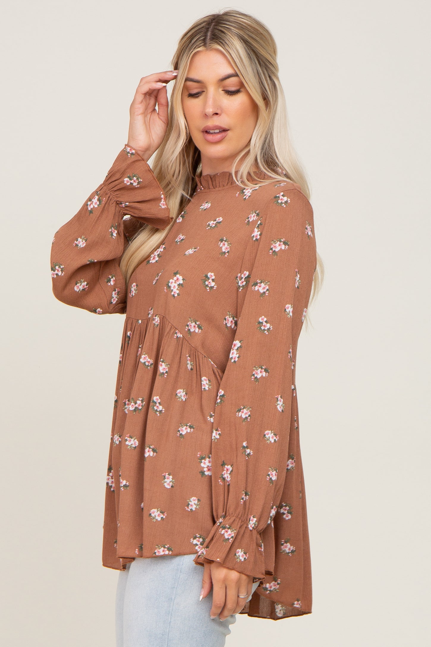 woman wearing a brown floral long sleeve top with a ruffled neckline and peplum hem, styled with light wash jeans
