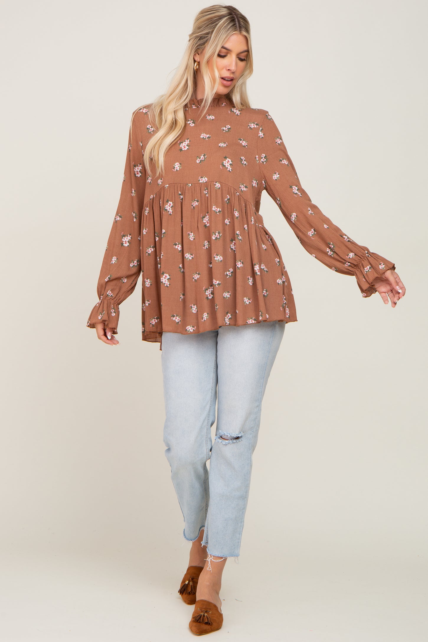 woman wearing a brown floral long sleeve peplum top paired with light blue distressed jeans and brown slip-on shoes