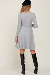 woman wearing a gray long sleeve maternity dress with a flared skirt and black knee-high boots, showing her back