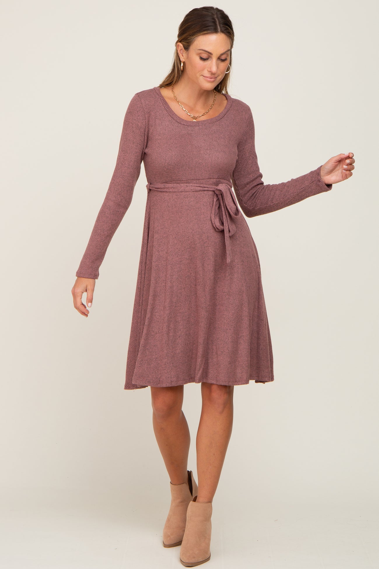 woman wearing a mauve long sleeve sweater dress with a belted waist and a flared skirt