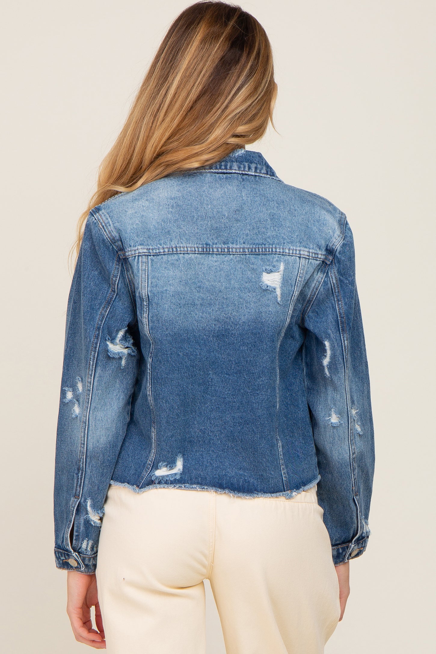 Back view of a woman wearing a distressed blue denim jacket with frayed hem and ripped details