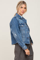 Woman wearing a distressed blue denim jacket with a raw hem and dark grey trousers