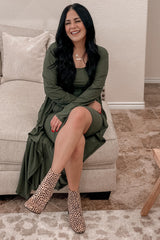 woman wearing an olive green long sleeve dress sitting on a couch, paired with leopard print ankle boots