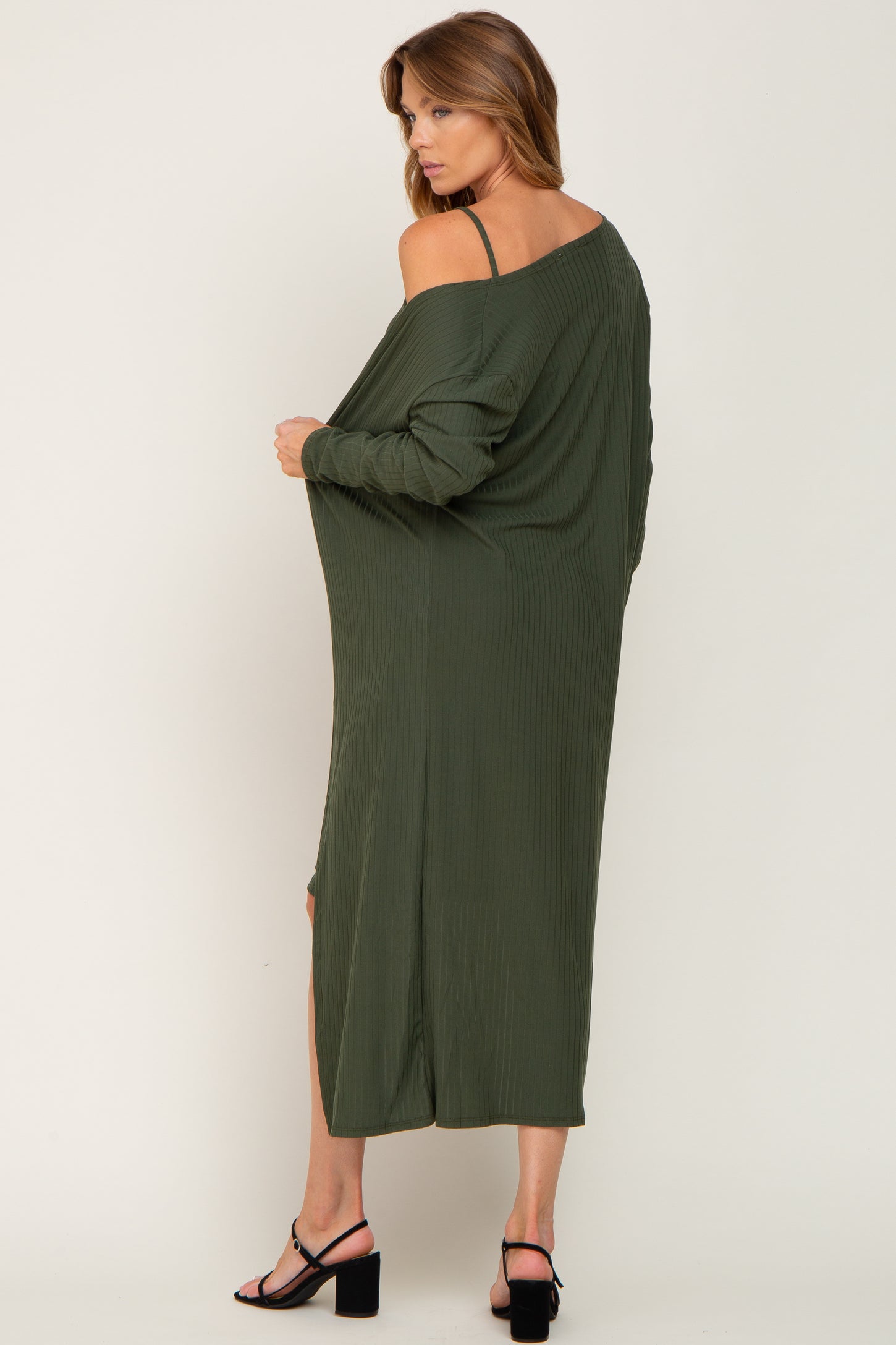 woman wearing a long olive green off-shoulder dress with side slits and a relaxed fit, standing with her back to the camera