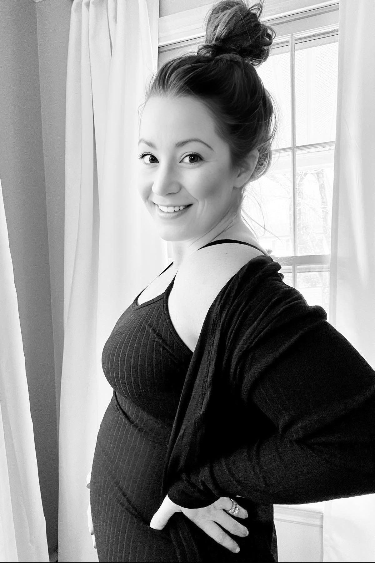 woman wearing a black striped maternity tank top and cardigan with a visible baby bump