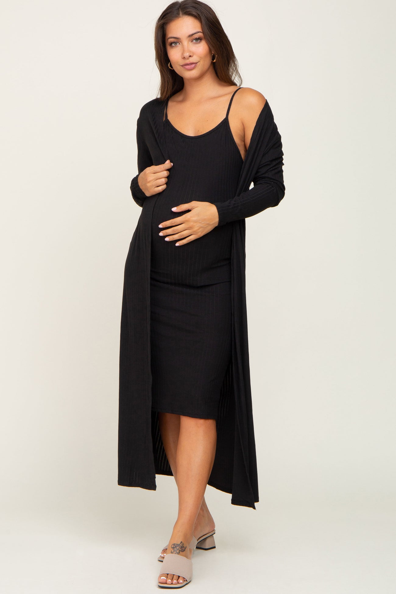 woman wearing a black ribbed maternity dress with a matching long cardigan and holding her baby bump