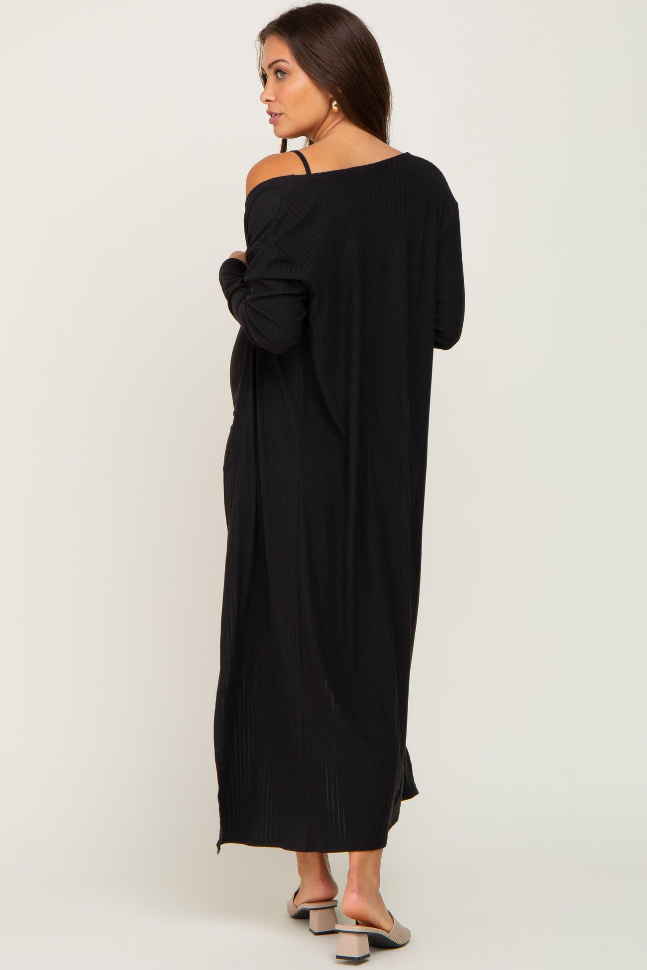 woman wearing a long black maternity dress with a relaxed fit and open back, showcasing her baby bump