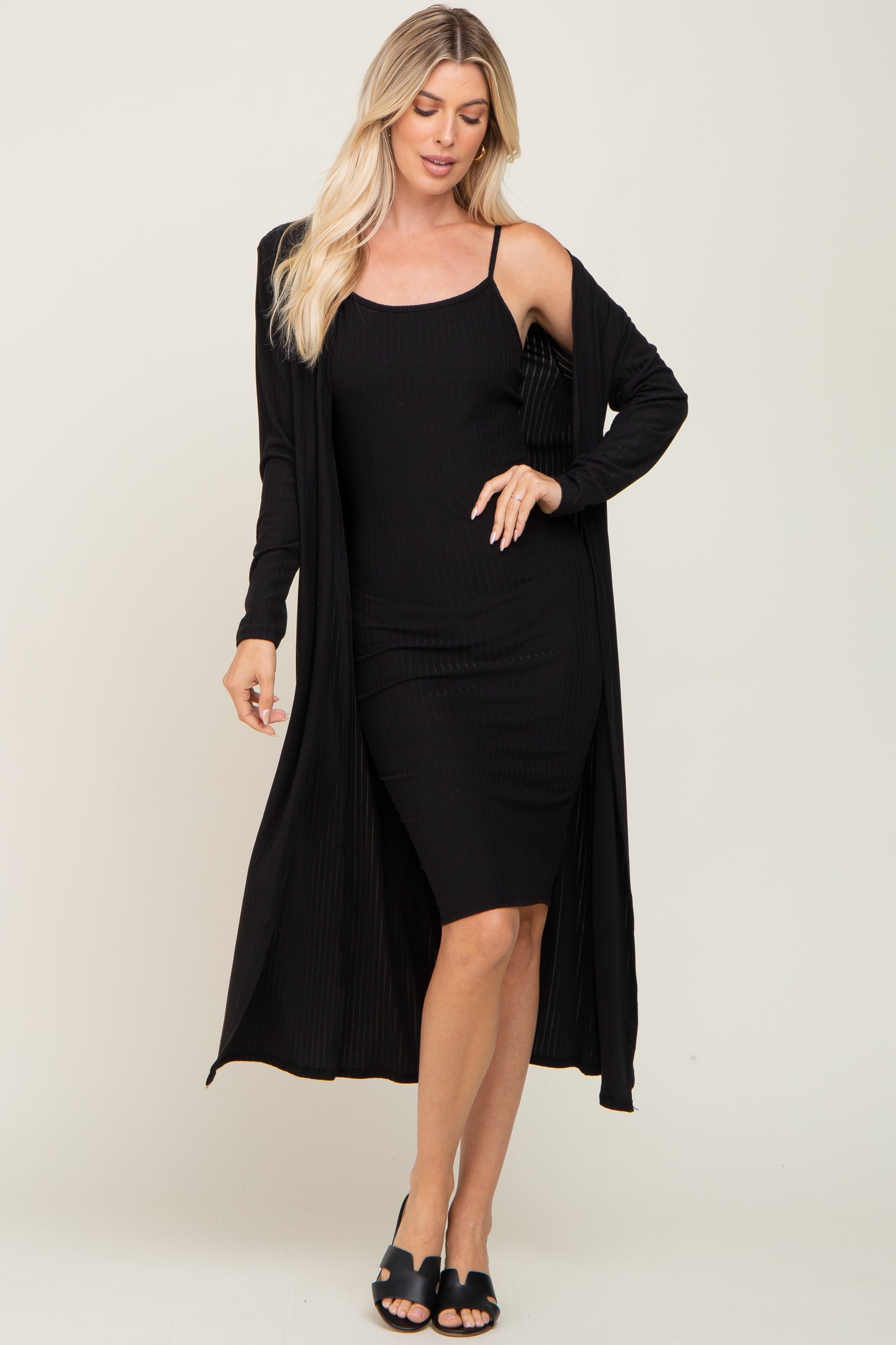 woman wearing a black ribbed tank dress with a long black cardigan over it and black slide sandals