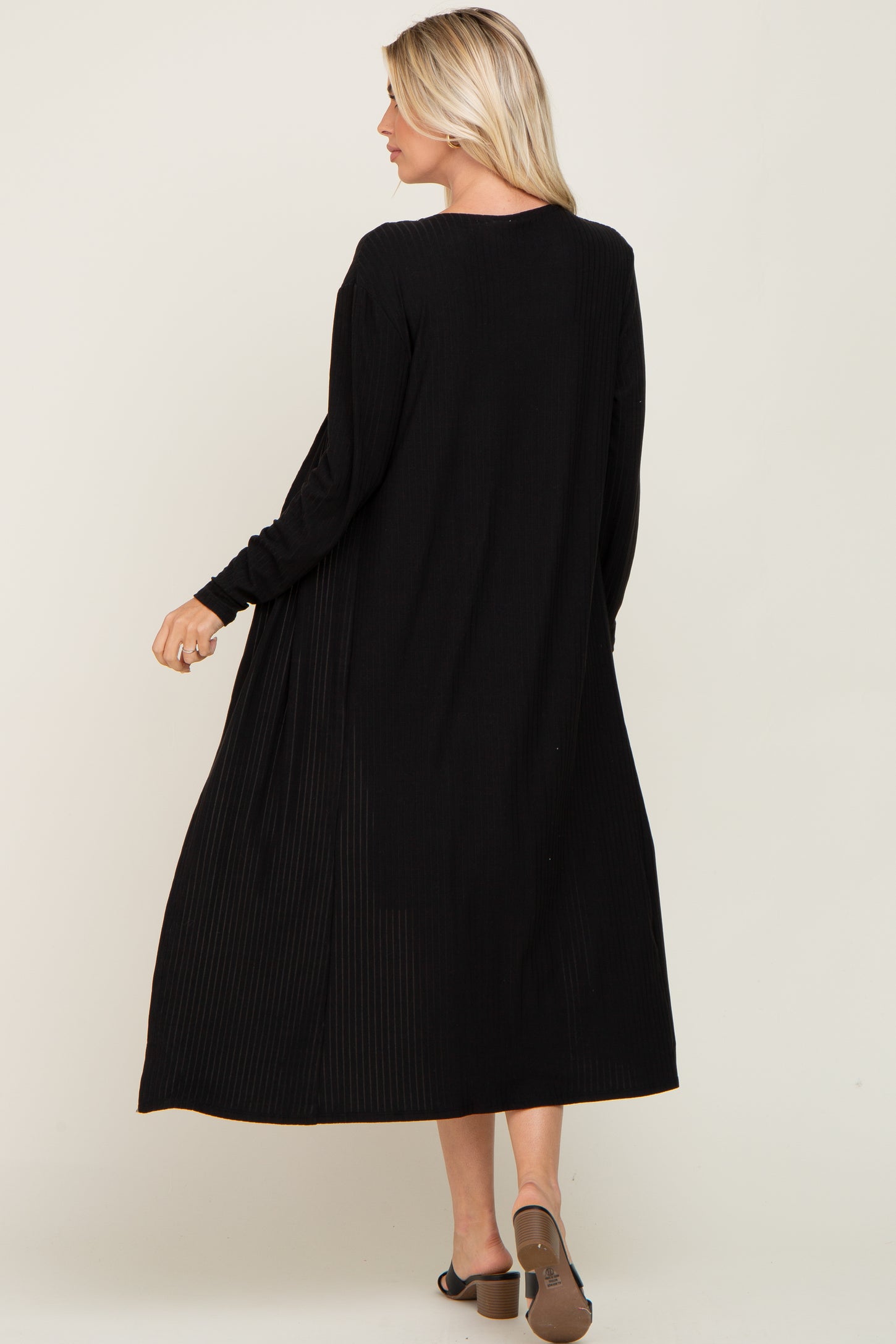woman wearing a black long sleeve maxi dress with pleated details, showing the back view