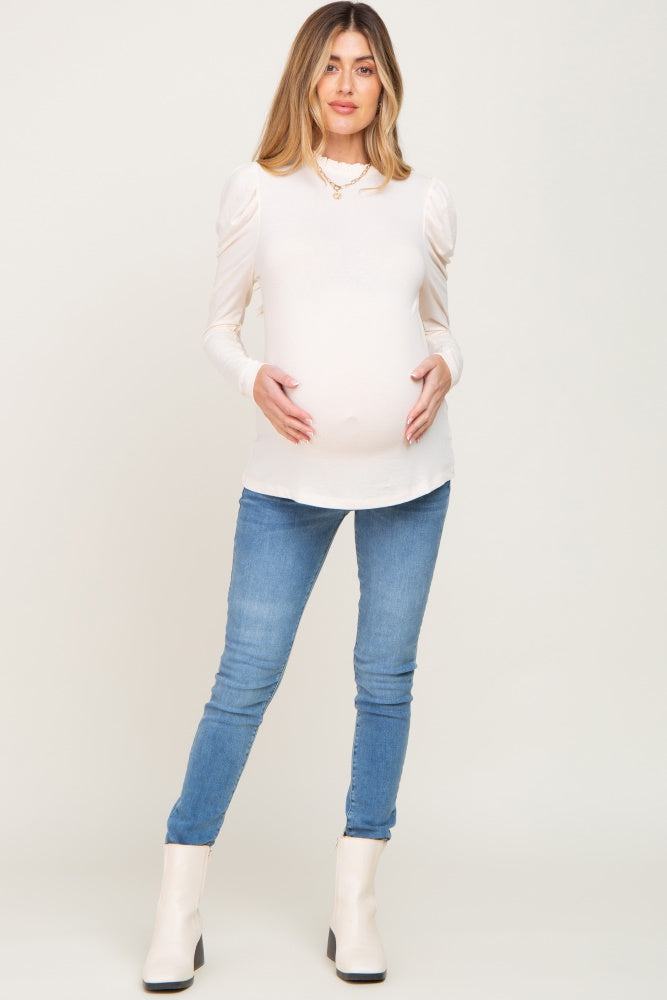 pregnant woman in cream puff sleeve maternity top and blue skinny jeans with white ankle boots