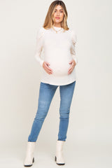 pregnant woman in cream puff sleeve maternity top and blue skinny jeans with white ankle boots