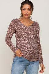 Woman wearing a purple floral long sleeve maternity henley top and light wash jeans