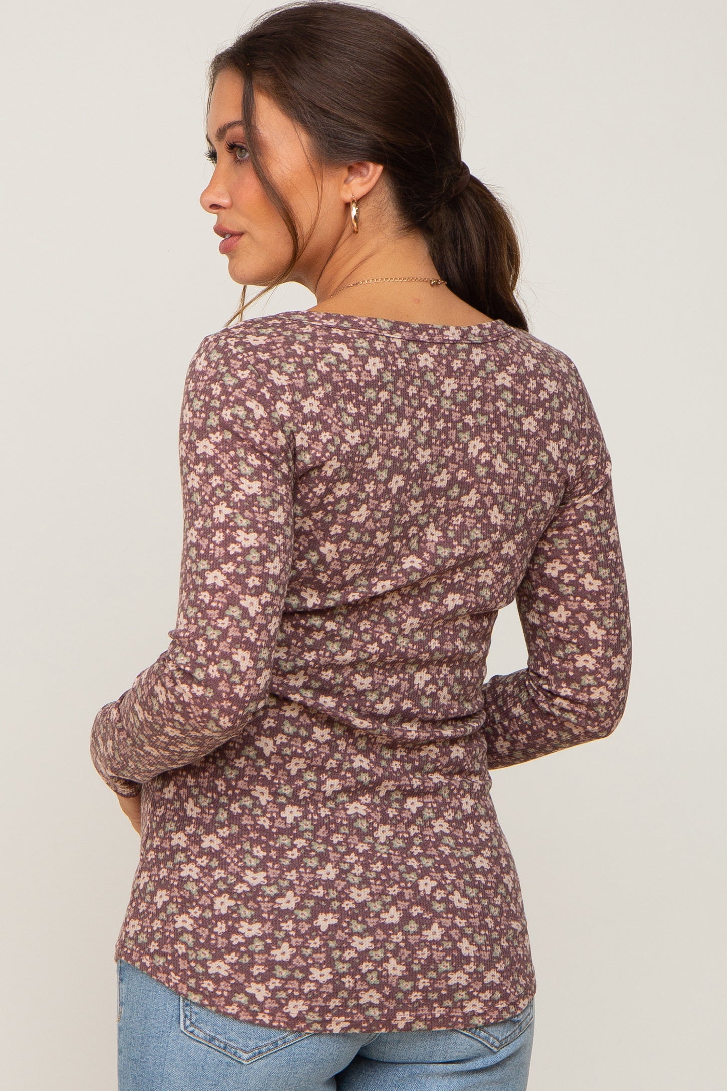 Woman wearing a long sleeve purple floral print ribbed top and blue jeans viewed from the back